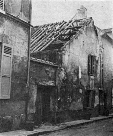 Vue depuis la rue d'une bâtisse basse à pignon sur rue à l'état de ruine. Le toit est totalement dépourvu de couverture et même les chevrons commencent à manquer. Les murs sont d'un aspect répugnant et lépreux.